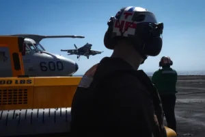 Một thành viên phi hành đoàn trên boong tàu sân bay của Hải quân Mỹ quan sát máy bay F/A-18 Super Hornet hạ cánh xuống tàu sân bay USS Theodore Roosevelt [Ảnh: Michelle Bir/AFP]